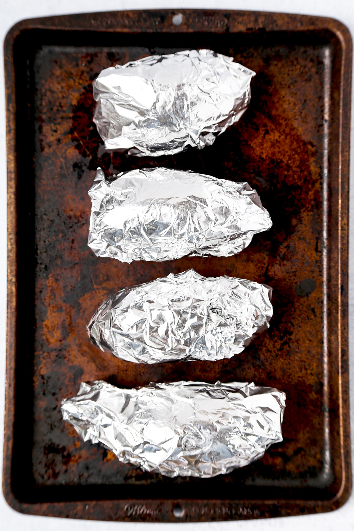 foil wrapped potatoes on cooking sheet